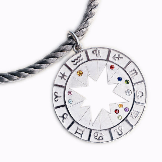 Der Astro Diamond Silber ist ein runder Anhänger (4,5 cm Durchmesser), der das persönliche Geburtshoroskop seines Trägers abbildet. In der Mitte strahlt ein ausgestanzter Stern, umgeben von den zwölf Tierkreiszeichen als feines Relief. Die Positionen der Himmelskörper zum Zeitpunkt der Geburt – Sonne, Mond und Planeten – werden durch echte Edelsteine markiert und machen jedes Stück zu einem einzigartigen Talisman.
